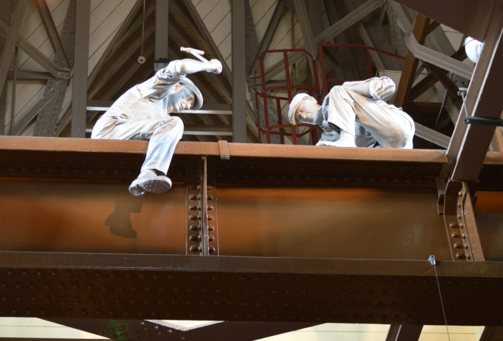 Two mannequin men in white apparel building a steel frame on Tower Bridge London England