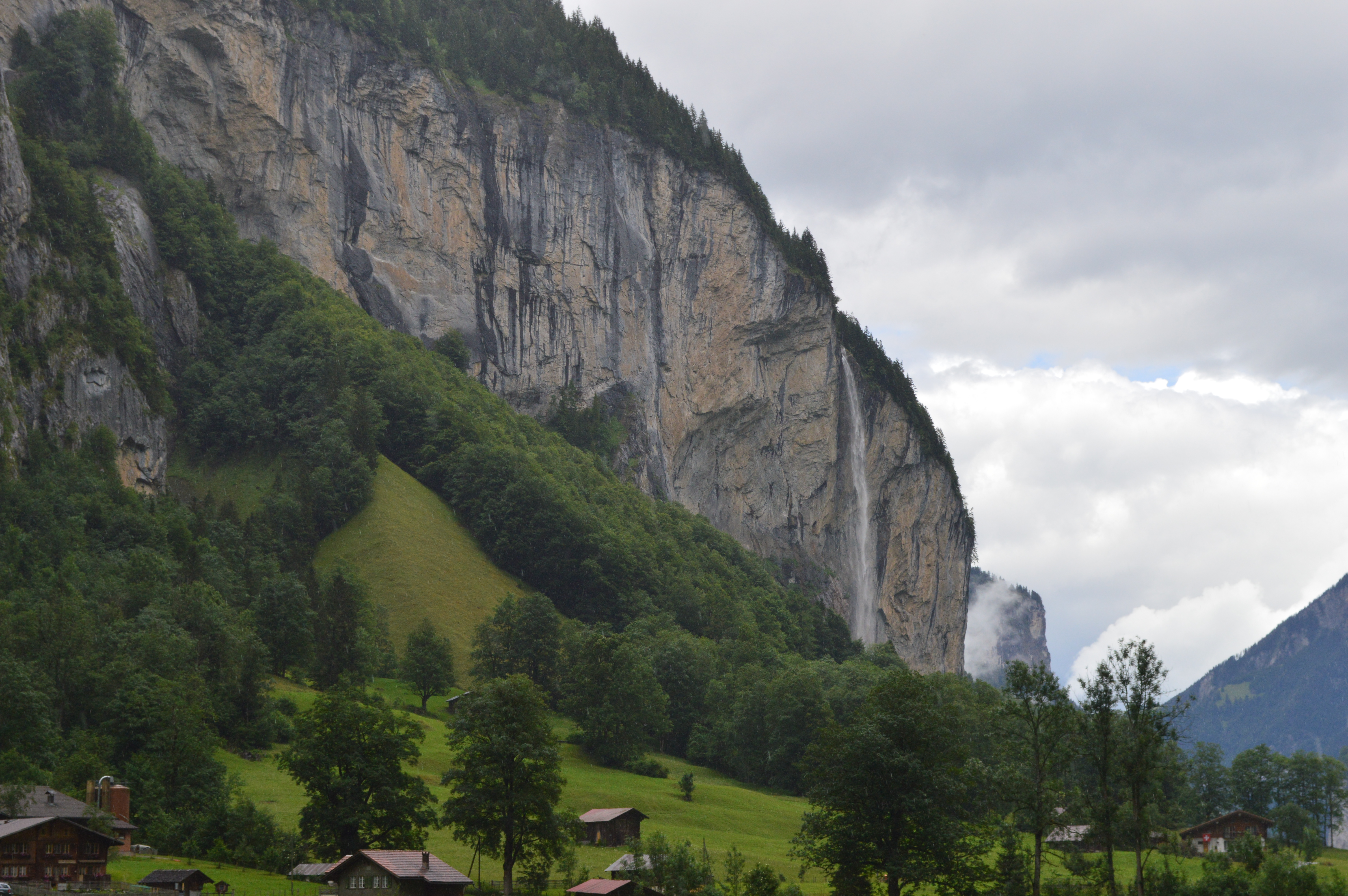 Waterfalls high on top of mountain flowing down to grass and trees in Lauterbrunnen, Switzerland