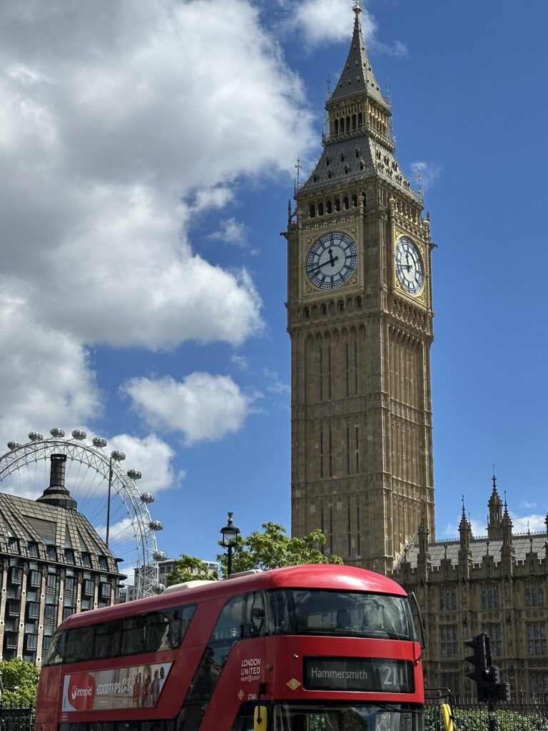 Big Ben with red bus in forefront and London Eye in background of blue sky in London, England